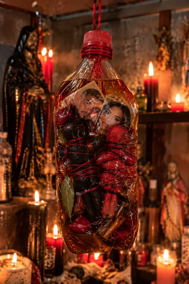 Trabajo de endulzamiento en botella de miel con las fotos de la pareja y dos figuras atadas con hilo rojo, canela y pétalos de rosa